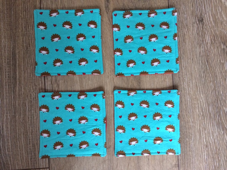 Pu&ograve; includere: Quattro sottobicchieri in tessuto blu turchese con un motivo ripetitivo di ricci marroni e cuori rossi.