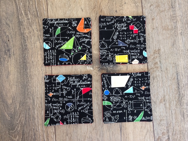 May include: Four black fabric coasters with a white mathematical formula and geometric shapes printed on them. The coasters have red stitching around the edges.