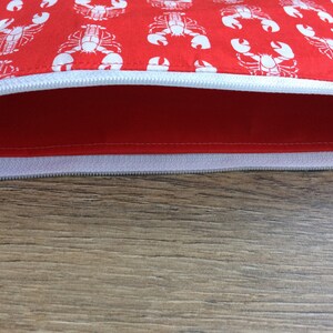 May include: A red zippered pouch with a white lobster print. The pouch is open and the zipper is visible.