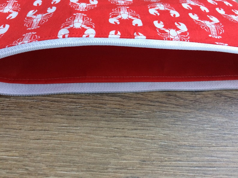 May include: A red zippered pouch with a white lobster print. The pouch is open and the zipper is visible.