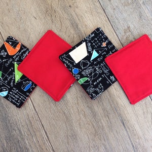 May include: Four coasters, two red and two black. The black coasters feature a white design of mathematical equations and symbols. The coasters are square shaped.