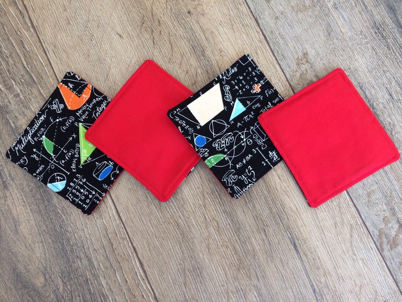 May include: Four coasters, two red and two black. The black coasters feature a white design of mathematical equations and symbols. The coasters are square shaped.