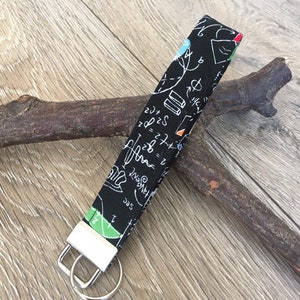 May include: Black and white fabric keychain with a white and green key ring. The fabric has a pattern of math equations and symbols.