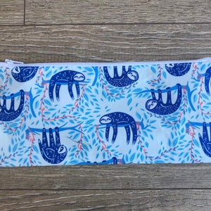 May include: A rectangular pencil case with a white zipper. The case features a repeating pattern of blue sloths hanging from branches with blue leaves and red vines on a white background.