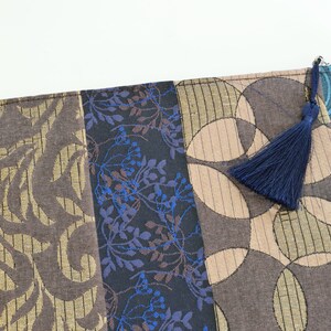 May include: A blue, brown and gold fabric zippered pouch with a blue tassel. The pouch is made of different patterned fabrics.