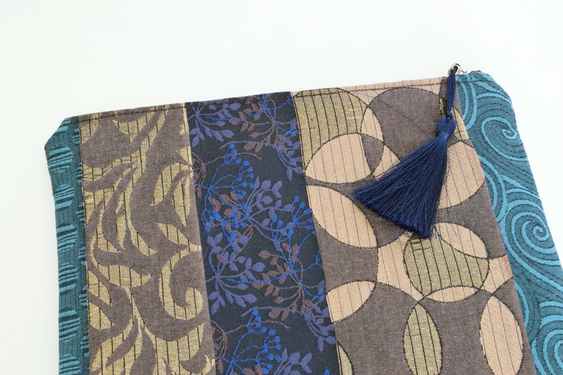 May include: A blue, brown and gold fabric zippered pouch with a blue tassel. The pouch is made of different patterned fabrics.