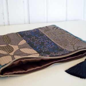 May include: A zippered pouch with a blue, brown and gold patterned fabric exterior. The pouch has a brown lining and a dark blue tassel.