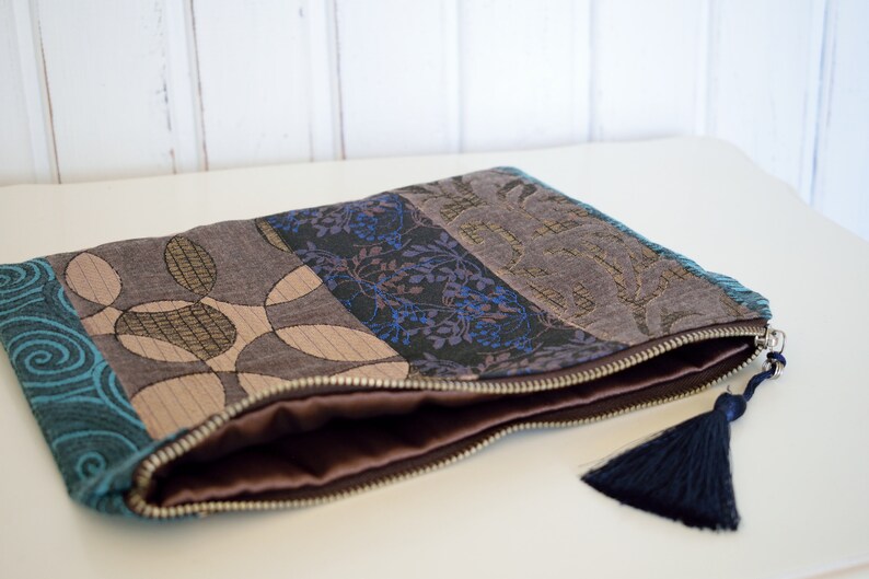 May include: A zippered pouch with a blue, brown and gold patterned fabric exterior. The pouch has a brown lining and a dark blue tassel.