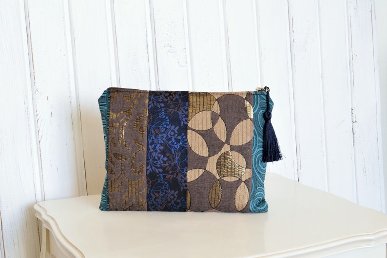 May include: A brown and blue patchwork clutch bag with a black tassel. The bag features a geometric pattern and a floral design.