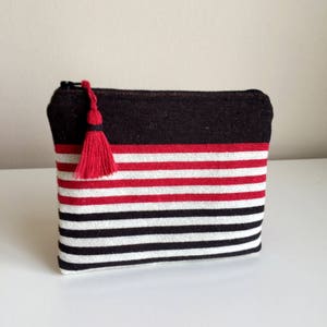 May include: A black and white striped zippered pouch with a red stripe and a red tassel.