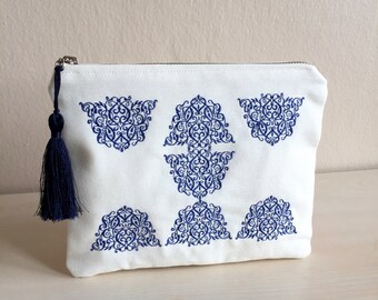 May include: White canvas zippered pouch with a blue tassel and intricate blue embroidered designs. The designs are geometric and floral.