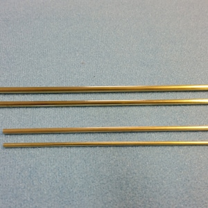 May include: Four gold-colored metal rods of varying lengths. The rods are arranged in a row from longest to shortest.