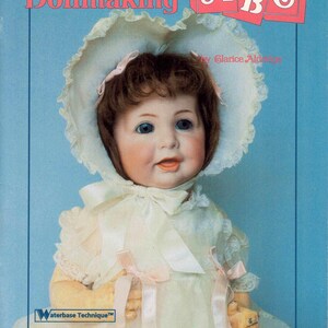 May include: A book titled "Porcelain Dollmaking ABC" by Glarice Aldridge. The cover features a porcelain doll wearing a white dress and a white bonnet with a pink ribbon. The book is a complete, step-by-step guide to dollmaking.