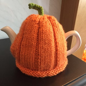 Puede incluir: Calienta-tetera de punto de color naranja en forma de calabaza con un tallo verde.