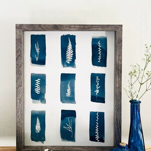May include: A framed print with nine blue watercolor squares, each featuring a white silhouette of a different type of leaf or plant.