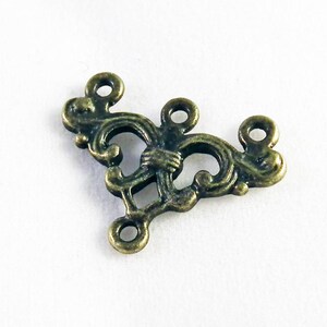May include: A gold-toned metal connector with a decorative, ornate design. It has three loops for attaching jewelry or other crafts.
