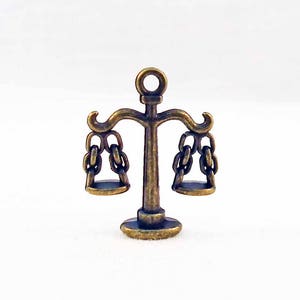 May include: A small, antique gold-toned metal scale charm with two hanging pans and a decorative base.