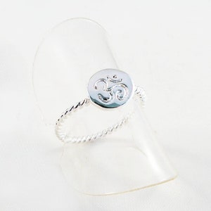 May include: A silver ring with a twisted band and a round, silver charm featuring an Om symbol.