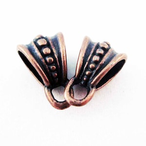 Op de afbeelding: Twee antieke koperkleurige metalen hangerbedels met een decoratieve parelrand. De bedels hebben een lus aan de bovenkant om een ​​ketting of koord aan te bevestigen.