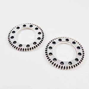 May include: Two silver metal rings with a toothed edge and small holes around the outer edge.