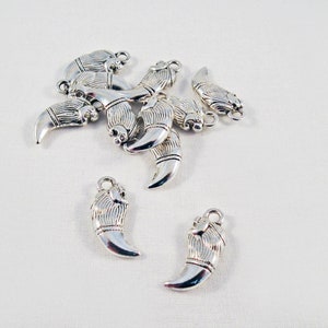 May include: A group of silver metal claw charms, some are clustered together, while others are spread out on a white surface.