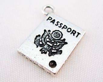 Könnte beinhalten: Ein silberfarbener Reisepass-Anhänger mit dem Wort "PASSPORT" in schwarzer Schrift. Der Anhänger zeigt ein detailliertes Emblem und ein kleines Loch. Der Anhänger ist ein Accessoire zum Thema Reisen.