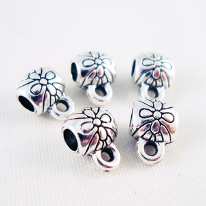 May include: Five silver-toned metal end caps with a floral design. Each cap has a small loop for attaching to a cord or string.