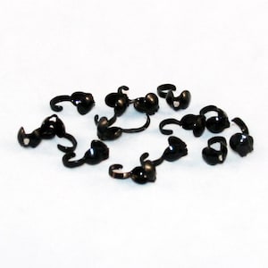 以下が含まれることがあります： ジュエリー作りに使用される、黒い金属製のクリンプビーズのグループです。
