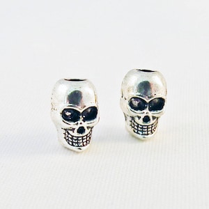 May include: Two silver skull beads with black eye sockets and a toothy grin.