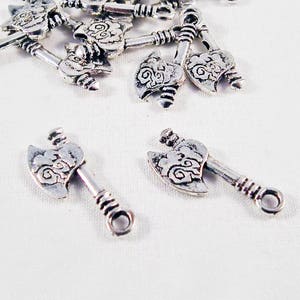 May include: A group of silver-toned axe charms with intricate designs. The charms are scattered on a white surface.