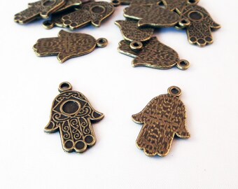 May include: A group of 14 bronze hamsa hand charms with an eye in the center. The charms are arranged in a pile on a white background.