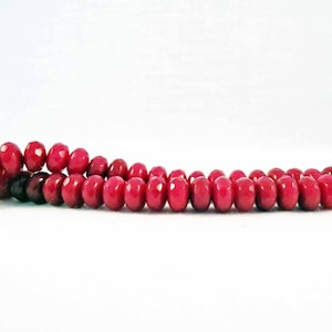 Peut inclure: Un rang de perles ovales et facettées d'un rouge profond. Les perles sont enfilées ensemble, créant un collier ou un bracelet. Le fond est blanc uni, mettant en valeur la couleur et la forme des perles.