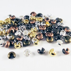 May include: A pile of small, metal, open jump rings in silver, gold, and bronze colors. The rings are used for jewelry making.