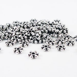 May include: A large pile of silver-toned metal flower-shaped beads. The beads have a small hole in the center and are about 1/2 inch in diameter.