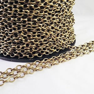 May include: A spool of brass chain, with a section of the chain uncoiled and lying flat on a white surface. The chain is a classic oval link style.