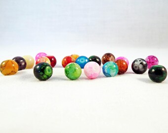 May include: A collection of colourful agate beads with various patterns and swirls. The beads are round and smooth, with a glossy finish. They are arranged in a row on a white surface.