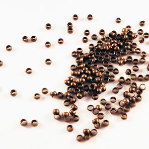 May include: A large pile of small, round, bronze-colored metal crimp beads. The beads are scattered on a white surface.