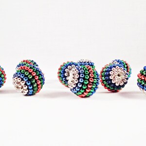 Peut inclure: Six petites perles rondes multicolores avec un centre argenté. Les perles sont composées de petites perles rondes dans des tons de rouge, vert, bleu et argent.