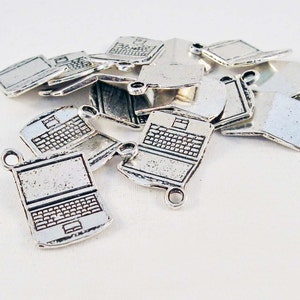 Puede incluir: Un montón de dijes de metal plateado en forma de computadora portátil. Los dijes tienen forma de computadoras portátiles con teclado y pantalla. Los dijes tienen un bucle en la parte superior para sujetarlos a un collar o pulsera.