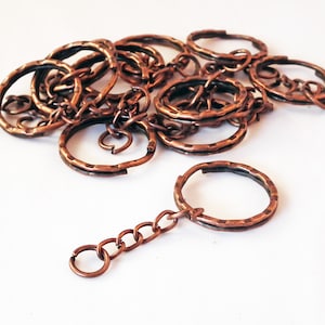 May include: A pile of copper key rings with a single copper key chain attached. The key rings are all the same size and have a hammered finish.