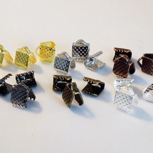 May include: Assortment of metal clasps in various finishes, including gold, silver, black, and copper. The clasps have a square shape with a textured surface and a small loop on the top.
