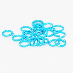 May include: A pile of small, light blue metal jump rings. The rings are all the same size and are arranged in a loose pile.