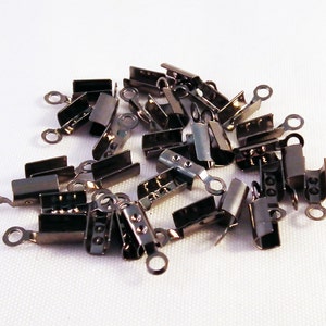 May include: A pile of black metal cord end caps with a small loop on one end. The caps are designed to secure the end of a cord or rope.