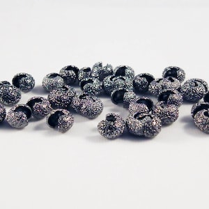 May include: A close-up of a pile of small, black metal beads with a textured surface. The beads are designed to be used as end caps for jewelry making.
