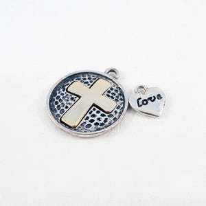 May include: Silver charm with a gold cross on a textured round pendant and a silver heart charm with the word "Love" engraved on it.