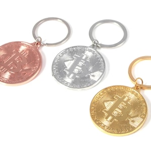 May include: Three keychains with a Bitcoin symbol on a round metal charm. The charms are gold, silver, and rose gold.
