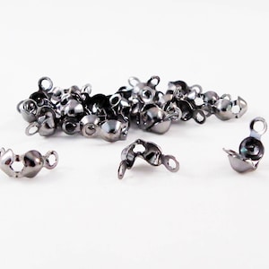 Puede incluir: Un conjunto de terminales de cuentas de crimpado de color metal de cañón, utilizados para la fabricación de joyas. Las tapas son pequeñas, con forma redondeada y un lazo para sujetar a una cadena o cordón.