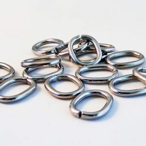 Peut inclure: Un ensemble de anneaux de saut ovales de couleur argentée. Ces anneaux métalliques sont ouverts, avec un petit espace pour se fixer à d'autres composants de bijoux. Les anneaux sont dispersés sur une surface blanche.