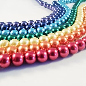 May include: A rainbow of pearl beads strung together in a long strand. The beads are arranged in a gradient from dark blue to red.