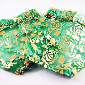 May include: Two green and gold organza gift bags with a floral pattern. The bags are made of sheer fabric with a gold rose design.